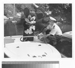 Disney mascot Mickey Mouse standing on a boat as a U.S. Coast Guard Auxiliary member attaches a decal